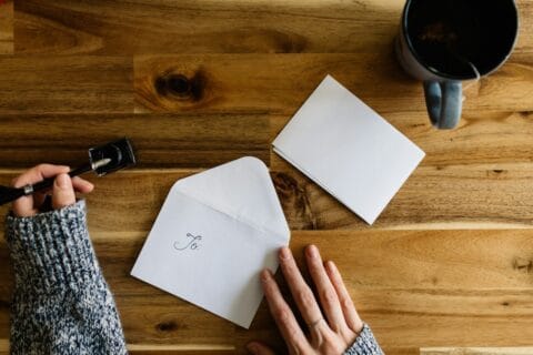 Manos junto a un sobre y una hoja en blanco sobre una mesa de madera, listas para escribir a la redacción